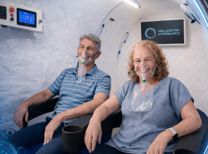 Two people relaxing in a Wellington Hyperbarics chamber while breathing oxygen through individual masks